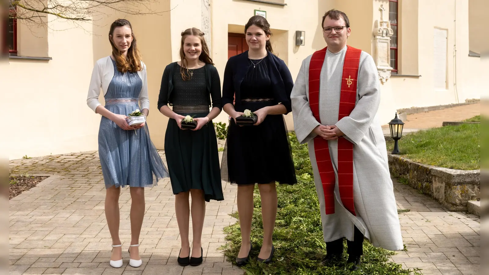 Die drei Konfirmandinnen mit Diakon René van Drongelen (von links) vor der Heilig-Kreuz-Kirche in Geilsheim.  (Foto: Beate Kißlinger/Fotostudio)