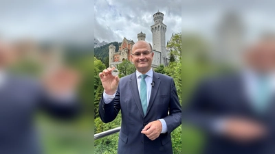 Finanzminister Albert Füracker (CSU) mit dem „Bayern Thaler“ in der Hand vor Schloss Neuschwanstein. (Foto: -/Bayerisches Finanzministerium/dpa)