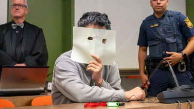 Der Angeklagte verbirgt sein Gesicht hinter einem Blatt Papier. (Foto: Peter Kneffel/dpa)
