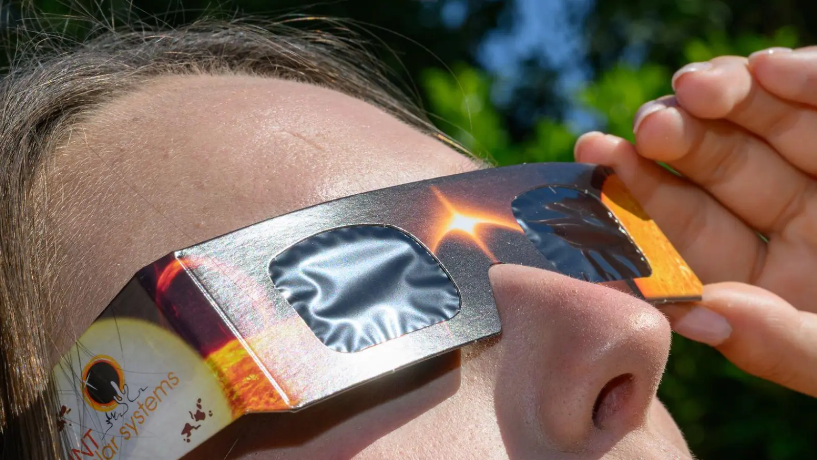 Eine junge Frau schaut durch eine Sonnenfinsternisbrille und betrachtet die Mittagssonne. (Foto: Patrick Pleul/dpa)
