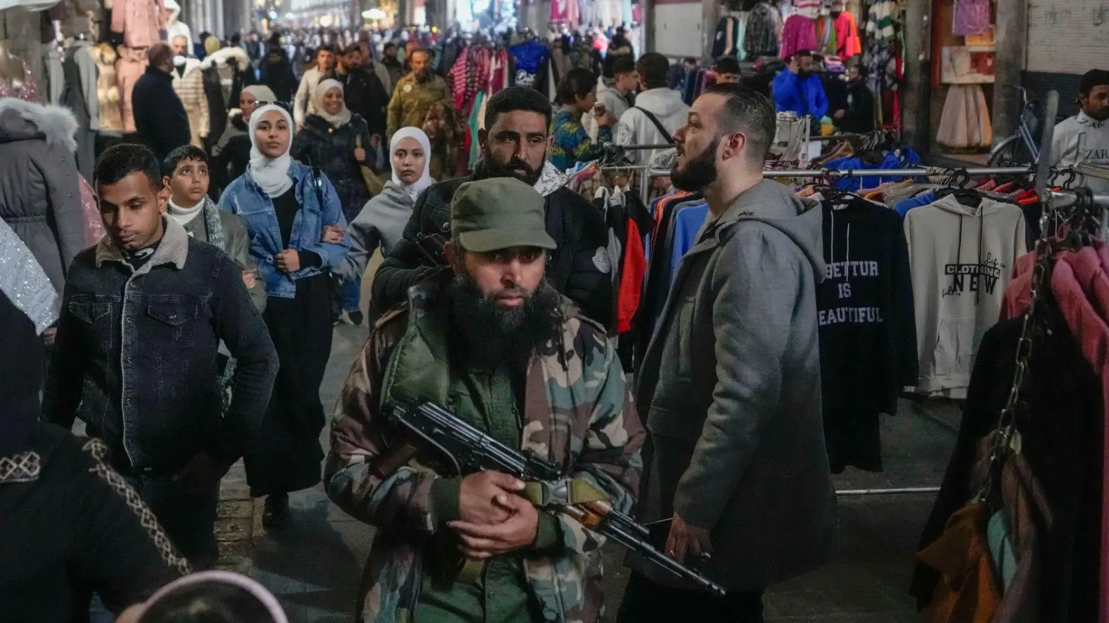 Ein Oppositionskämpfer geht zwischen Kunden in Damaskus über den Markt (Foto: Hussein Malla/AP/dpa)