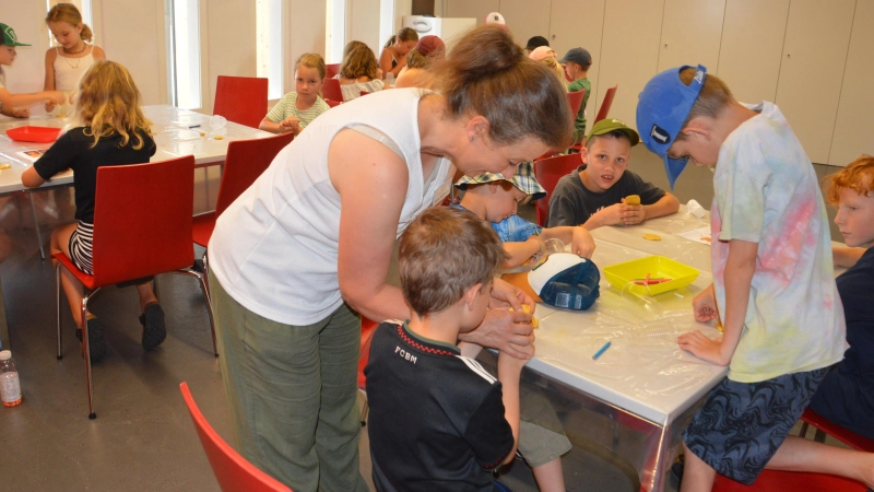 Kinder aus den Gemeinden rund um den Römerpark bastelten ihre eigenen Glücksbringer im Mehrzweckraum des Limeseums. Maike Schneider erklärt den Mädchen und Jungen nicht nur, wie das geht, sondern auch die Bedeutung, die im antiken Rom dahinter steckte. (Foto: Peter Tippl)