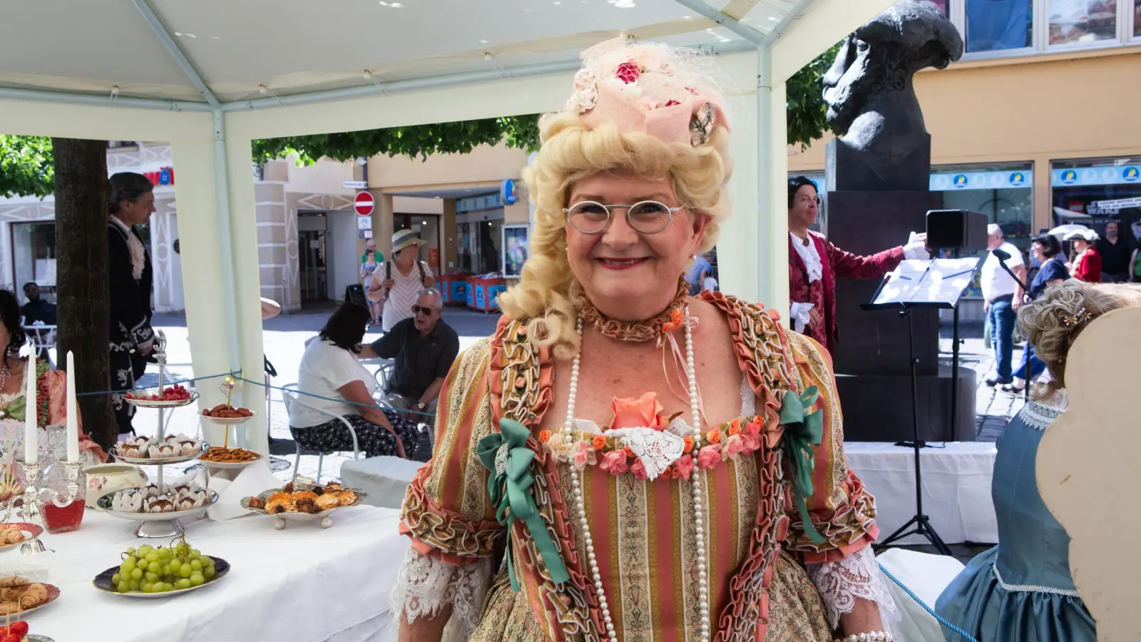 Vor der Sonne geschützt: Eine kostümierte Akteurin der Tanzgruppe Les Cotillons steht unter dem Dach des Pavillons. (Foto: Evi Lemberger)