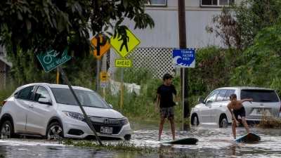 Zwei Jugendliche surfen in Waialua neben einem liegengebliebenen Fahrzeug im Hochwasser. (Foto: Stephen Lam/San Francisco Chronicle via AP/dpa)
