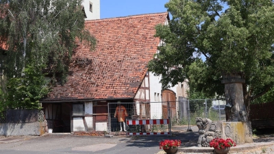Ein Bauzaun sichert einen Bereich vor dem alten Feuerwehrgerätehaus in Altmannshausen. An der Ecke, an der bereits Mauerwerk herausgefallen ist, wurde eine lebensgroße Puppe mit Warnkleidung ins Gebäude gestellt. (Foto: Andreas Reum)