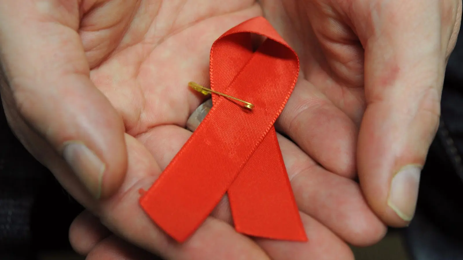 Ein mit dem HI-Virus infizierter Mann mit einer roten Schleife als Symbol der Solidarität mit HIV-Positiven und Aids-Kranken. (Foto: Arne Dedert/dpa)