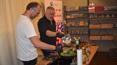 Schriftsteller Peter Denlo (rechts) bot in der Feuchtwanger Stadtbücherei bei der Lesung seines Buchs „Zungentod – Ein Burma-Krimi mit Rezepten“ auch etwas für den Gaumen. Beim Kochen am Wok bekam er mit Oliver Keil (links) Unterstützung aus dem Publikum.  (Foto: Erich Herrmann)