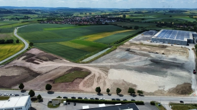 Das Areal, auf dem TransnetBW sein Zentrallager errichtet, gehört zum Gemeindegebiet Gebsattel. Auf der Drohnenaufnahme ist das Dorf im Hintergrund zu erkennen. Links verläuft die Kreisstraße nach Neusitz. Im Vordergrund ist die ins Rothenburger Gewerbegebiet führende Erlbacher Straße zu sehen. Die Halle am rechten Bildrand, die aus dem Bestand des 2023 insolvent gegangenen Küchenplatten-Herstellers Lechner stammt, wird in die neue Nutzung einbezogen. (Foto: Stefan Zeller)