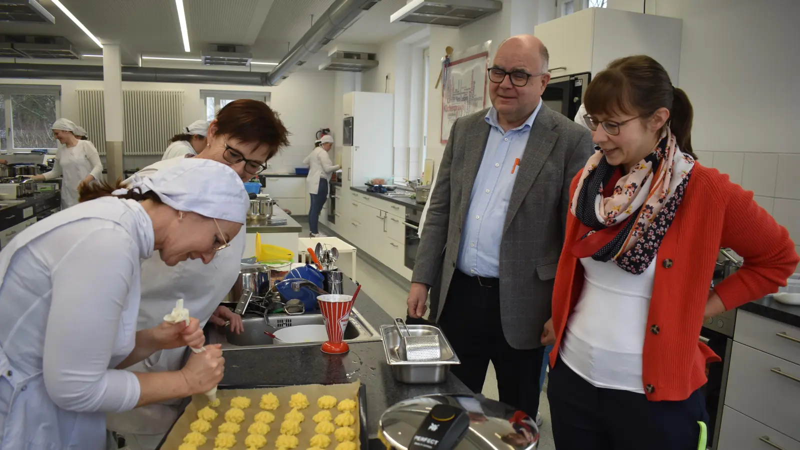 Schulleiter Norbert Pfeufer und Stellvertreterin Dr. Katharina Stenzel (rechts) sowie Lehrkraft Angelika Horn schauen einer Studentin bei der Zubereitung der Beilagen für den Sauerbraten über die Schulter. (Foto: Ute Niephaus)