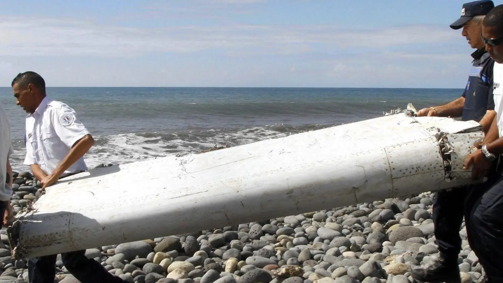 Techniker tragen ein Wrackteil, die Flügelklappe eines Flugzeugs, über einen Strand bei Saint-André,  Réunion. (Foto: Raymond Wae Tion/MAXPPP/QUOTIDIEN DE LA REUNION/dpa)