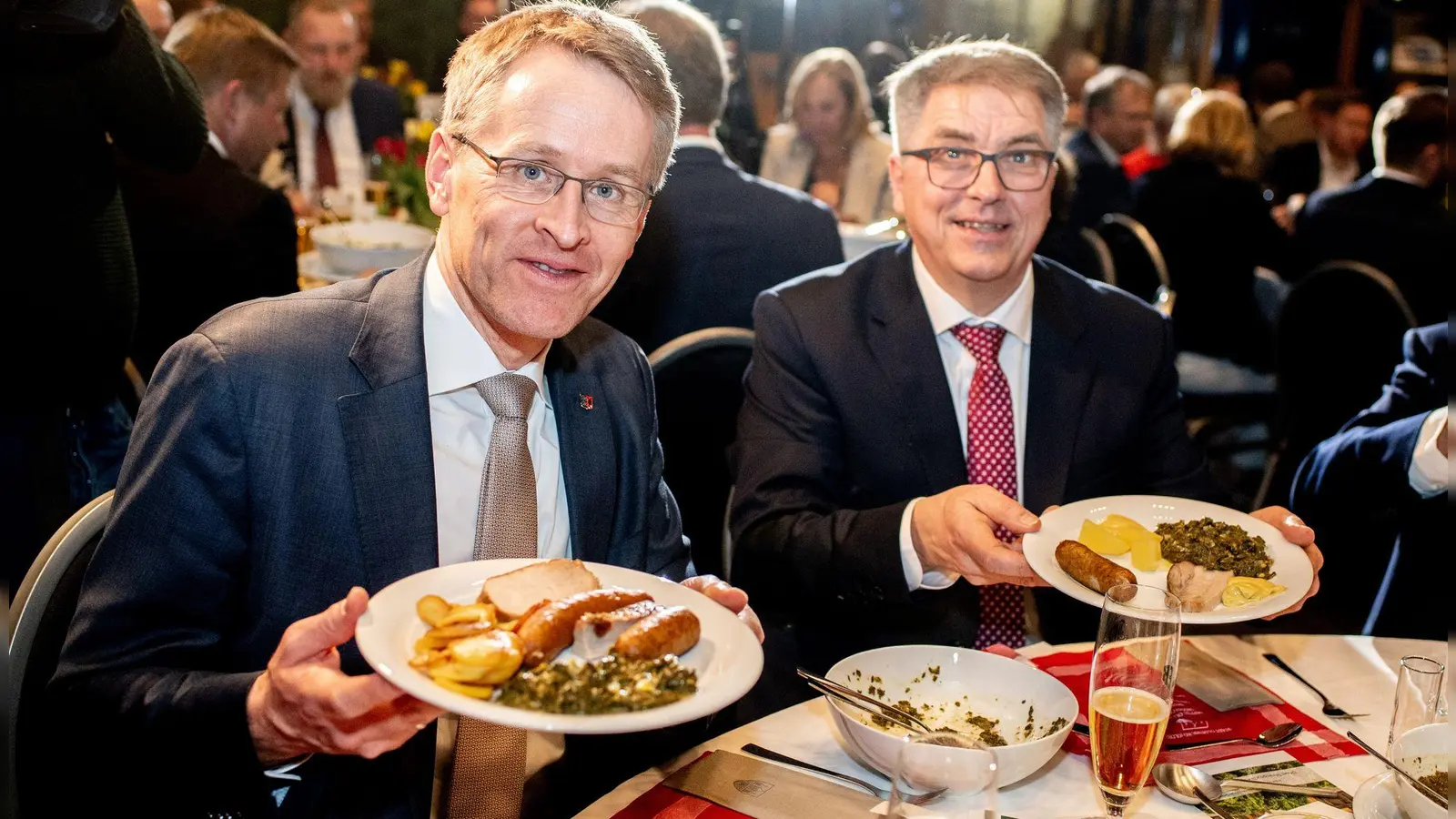 Daniel Günther (l), der Ministerpräsident von Schleswig-Holstein, ist der neue Oldenburger Grünkohlkönig. Hier beim Essen mit dem Oldenburger Oberbürgermeister Jürgen Krogmann (SPD). Auf den Tellern haben sie eine Portion Grünkohl und den klassischen Beilagen Kartoffeln, Pinkel, Kochwurst und Kassler. (Foto: Hauke-Christian Dittrich/dpa)