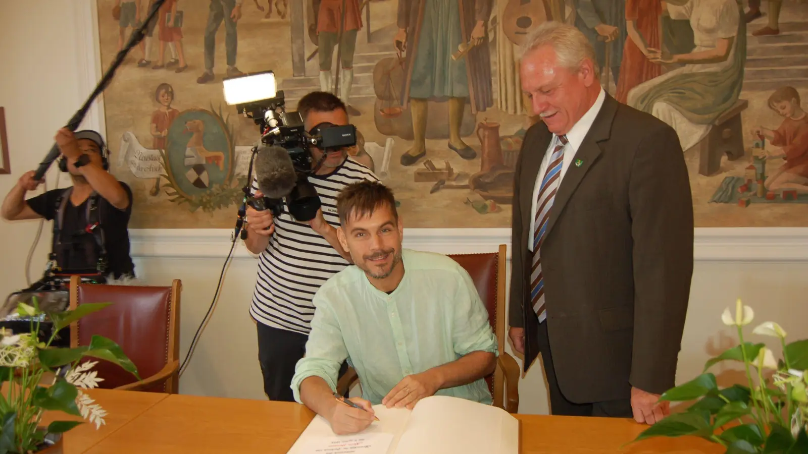 Nevio Passaro trug sich im Sitzungssaal des Neustädter Rathauses unter den Augen von Bürgermeister Klaus Meier ins Goldene Buch der Stadt ein. Ein Kamerateam des Bayerischen Rundfunks filmte mit. (Foto: Christa Frühwald)