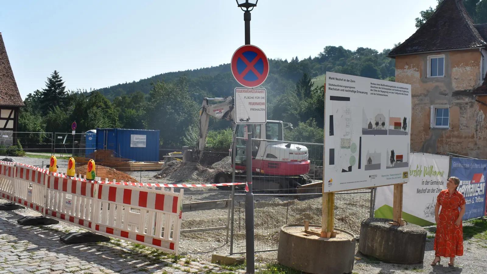 Neuhofs Bürgermeisterin Claudia Wust erläutert, wie die Remise auf dem Areal vor der Schlossscheune einmal aussehen soll. Mit den Arbeiten wurde begonnen. Bis Ende der Sommerferien sollen Tiefbauarbeiten und Bodenplatte fertig sein. Die Remise in Holzmodulbauweise wird danach errichtet. (Foto: Ute Niephaus)