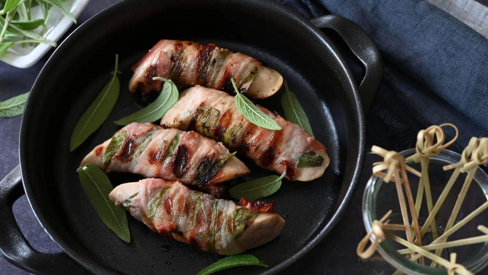 Ob in der Pfanne oder auf dem Grill: Umwickelt mit Salbeiblättern und Speck werden die Saltimbocca-Bratwürstchen garantiert zum Highlight.  (Foto: Julia Uehren/loeffelgenuss.de/dpa-tmn)