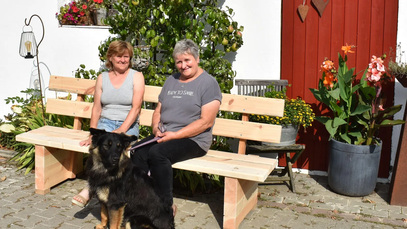 Jutta Zeller und Margit Bardenbacher (rechts) haben auf der Bank Platz genommen, die bald von ihrem neuen Eigentümer abgeholt wird. Er hatte sie beim Hoffest gewonnen. (Foto: Ute Niephaus)