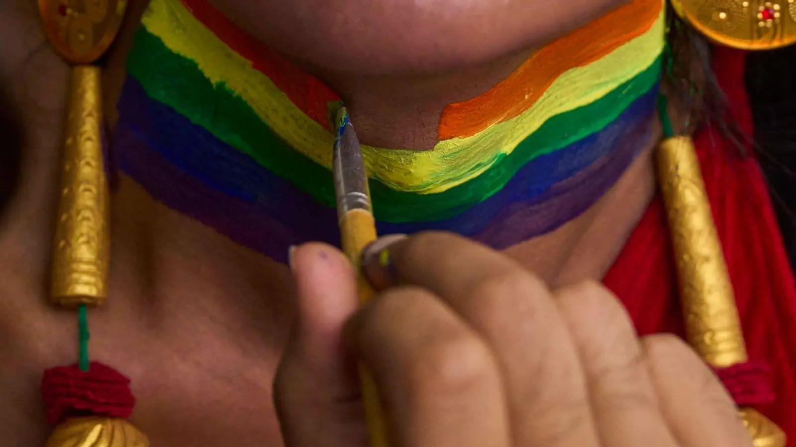 Eine Person bekommt den Hals in Regenbogenfarben für die Pride Parade in Kathmandu, Nepal bemalt. (Foto: Niranjan Shrestha/AP/dpa)