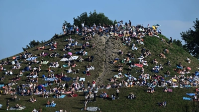 Erste Besucher bevölkern den Olympiaberg im Münchner Olympiapark, um von dort die partielle Sonnenfinsternis zu beobachten. (Foto: Felix Hörhager/dpa)