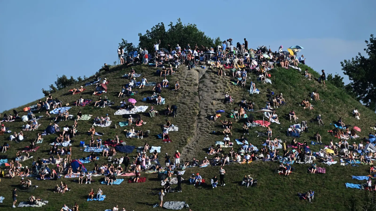 Erste Besucher bevölkern den Olympiaberg im Münchner Olympiapark, um von dort die partielle Sonnenfinsternis zu beobachten. (Foto: Felix Hörhager/dpa)