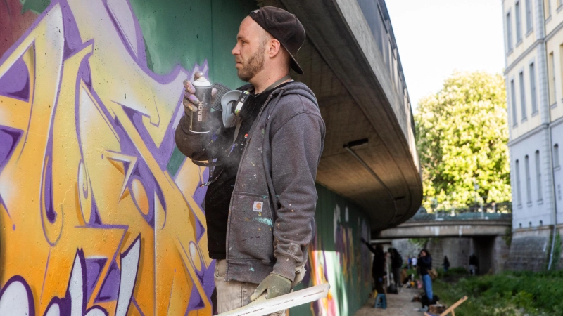 Verborgene Farbenpracht: Annähernd zwei Dutzend Künstlerinnen und Künstler (im Bild Fokus aus Fürth) haben mit ihren Bildern die Stützmauer an der Rezat farbenfroh gestaltet. Das 170 Meter lange Riesenkunstwerk ist allerdings von der Straße aus nicht zu sehen.  (Foto: Evi Lemberger)