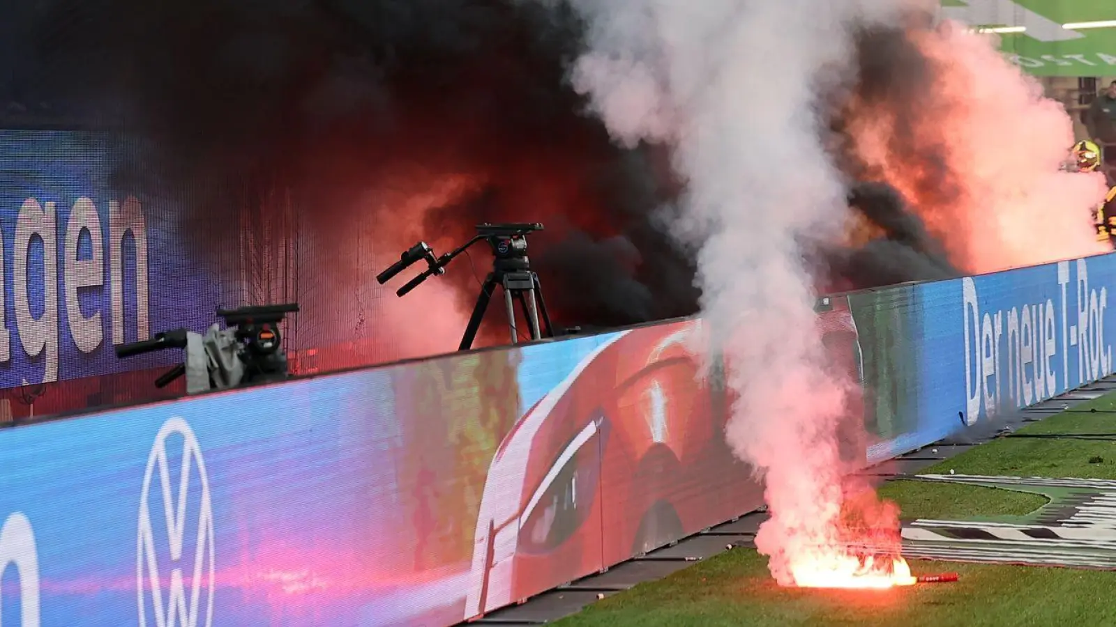  Fans von Wolfsburg werfen Leuchtfackeln auf den Platz. (Foto: Andreas Gora/dpa)