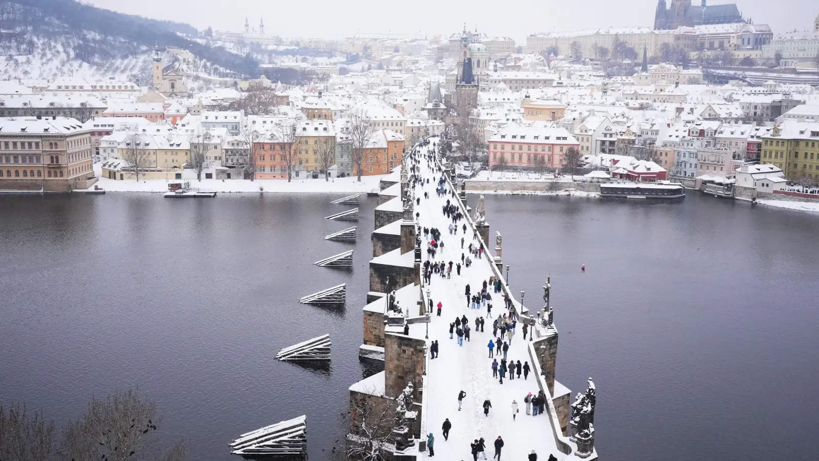 Menschen überqueren die mittelalterliche Karlsbrücke nach starkem Schneefall. (Foto: Petr David Josek/AP/dpa)