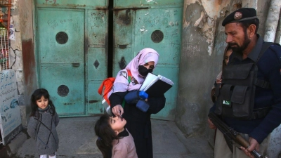 Ein Polizist in Pakistan steht Wache, während einem Kind ein Polio-Impfstoff verabreicht wird. (Foto: Muhammad Sajjad/AP/dpa)