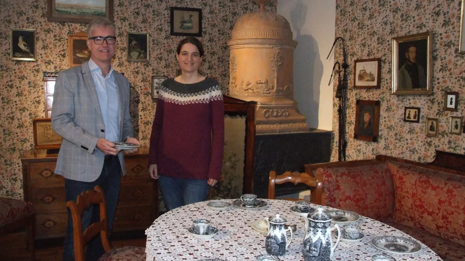 Eines der Epochenzimmer im Fränkischen Museum Feuchtwangen bietet einen Einblick in die Wohnkultur des Biedermeiers. Der Vorsitzende des Vereins für Volkskunst und Volkskunde, Bürgermeister Patrick Ruh, und Museumsleiterin Dr. Uta Karrer freuen sich auf die anstehende Sonderschau anlässlich „100 Jahre Dauerausstellung”. (Foto: Jasmin Kiendl)