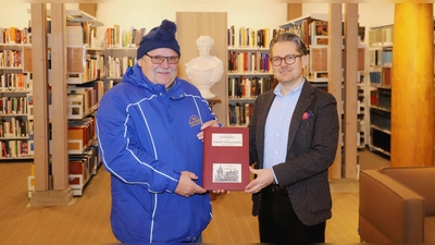Fritz Heubeck (links) übergibt Bibliotheksleiter Christian Mantsch ein Exemplar seines „Chronologischen Geschichtsbuchs des Ansbacher Weihnachtsmarktes”. (Foto: Oliver Herbst)