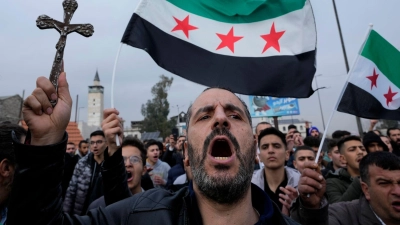 Ein syrischer Christ hält ein Kreuz hoch und ruft Parolen bei einem Protestmarsch in Damaskus, nachdem am Montagabend Unbekannte in Al-Sukailabija in der syrischen Provinz Hama den Weihnachtsbaum in Brand gesetzt hatten. (Foto: Hussein Malla/AP/dpa)