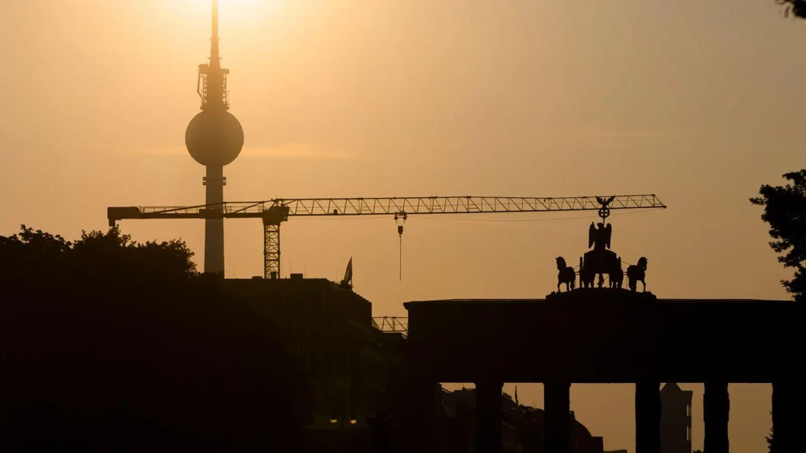 Das Brandenburger Tor und der Fernsehturm sind im Gegenlicht der aufgehenden Sonne zu sehen. Am Montag zeigt sich laut Vorhersage meist die Sonne, höchstens wird es locker bewölkt. (Foto: Christoph Soeder/dpa)