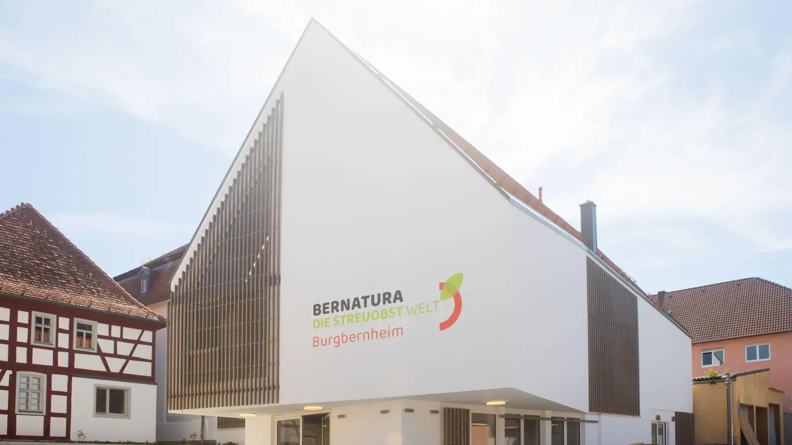 Mitten im Ort bietet der Neubau genügend Platz für eine Mosterei im Untergeschoss, einen Saal und weitere Funktionsräume. Im hinteren Bereich ist er mit zwei sanierten alten Fachwerk-Häusern (links) verbunden. (Foto: Evi Lemberger)
