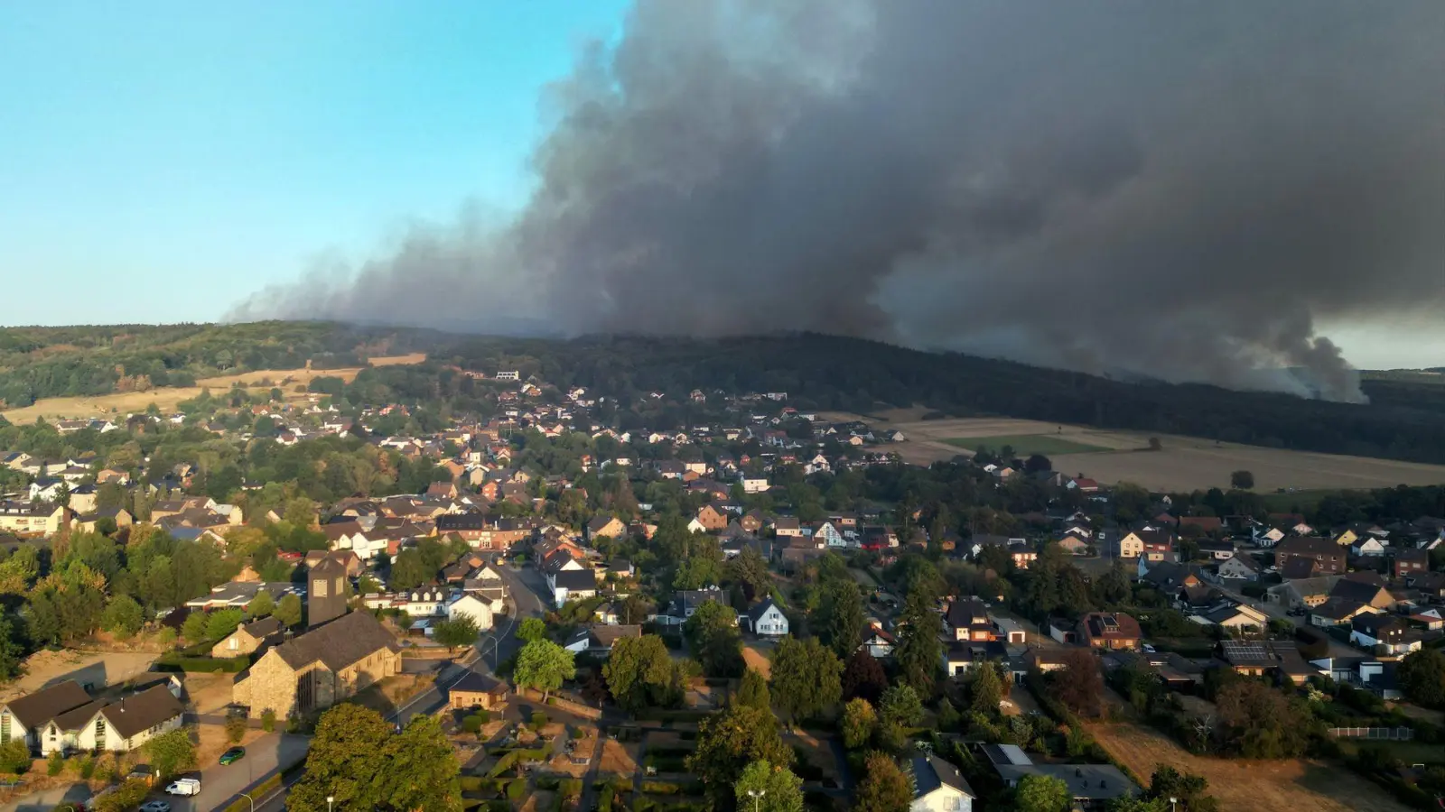 Rauch eines Waldbrands zieht über den Ortsteil Gey: Wenn das eigene Haus durch die Flammen Schaden nimmt, können Eigentümerinnen und Eigentümer auf ihre Wohngebäudeversicherung bauen. (Foto: Federico Gambarini/dpa/dpa-tmn)