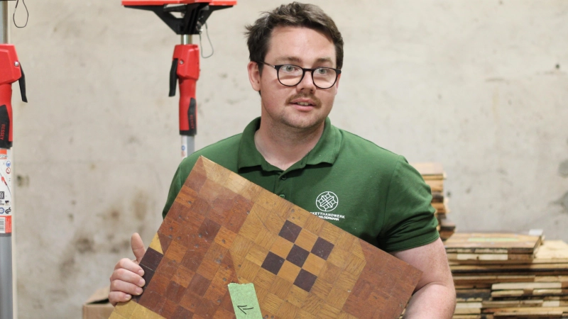 Parkettlegermeister und Restaurator Lars Wildermann aus Hohlach zeigt eine der unzähligen Parketttafeln, die auf die Restaurierung warten. (Foto: Constantin Prosch)