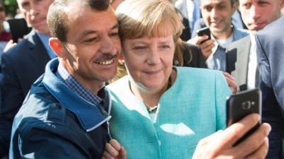Bald zehn Jahre her: Angela Merkel (CDU) lässt sich nach dem Besuch einer Erstaufnahmeeinrichtung für Asylbewerber in Berlin-Spandau für ein Selfie zusammen mit einem Flüchtling fotografieren. (Archivbild) (Foto: Bernd von Jutrczenka/dpa)