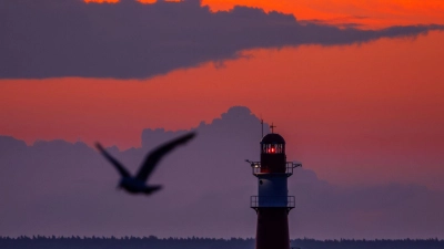 Die aufgehende Sonne färbt den Himmel hinter dem Leuchtfeuer auf der Ostmole am Ostseestrand von Warnemünde orangerot. (Foto: Jens Büttner/dpa)