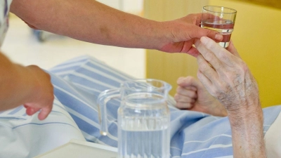 Eine Krankenpflegerin reicht einem Patienten ein Glas Wasser. (Foto: Daniel Karmann/dpa/Archivbild)