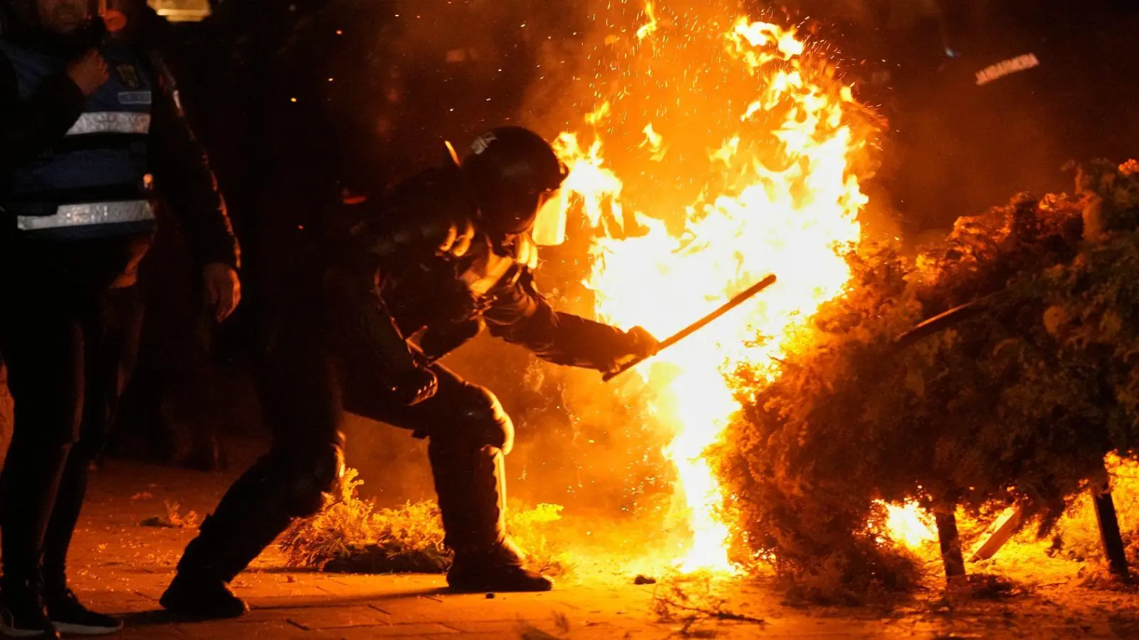 Die Polizei versucht, ein Feuer zu löschen, während Anhänger von Calin Georgescu protestieren. Die rumänische Wahlbehörde hat seine Kandidatur bei der Wiederholung der Präsidentschaftswahlen in Rumänien abgelehnt. (Foto: Vadim Ghirda/AP/dpa)