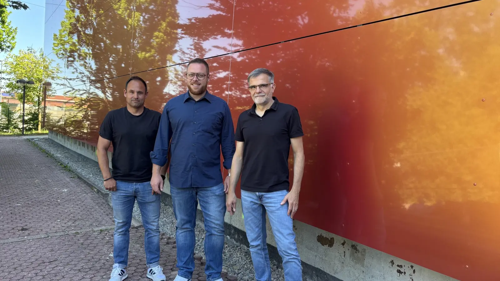 Bunt und spiegelnd ist die neue Fassade der Markgrafenhalle. Über den gelungenen Abschluss des vorletzten Bauabschnittes freuen sich (von links): Bauamtsmitarbeiter Frank Maes, Bürgermeister Alexander Müller und Bauamtsleiter Gerald Schorr. (Foto: Nicole Gunkel)