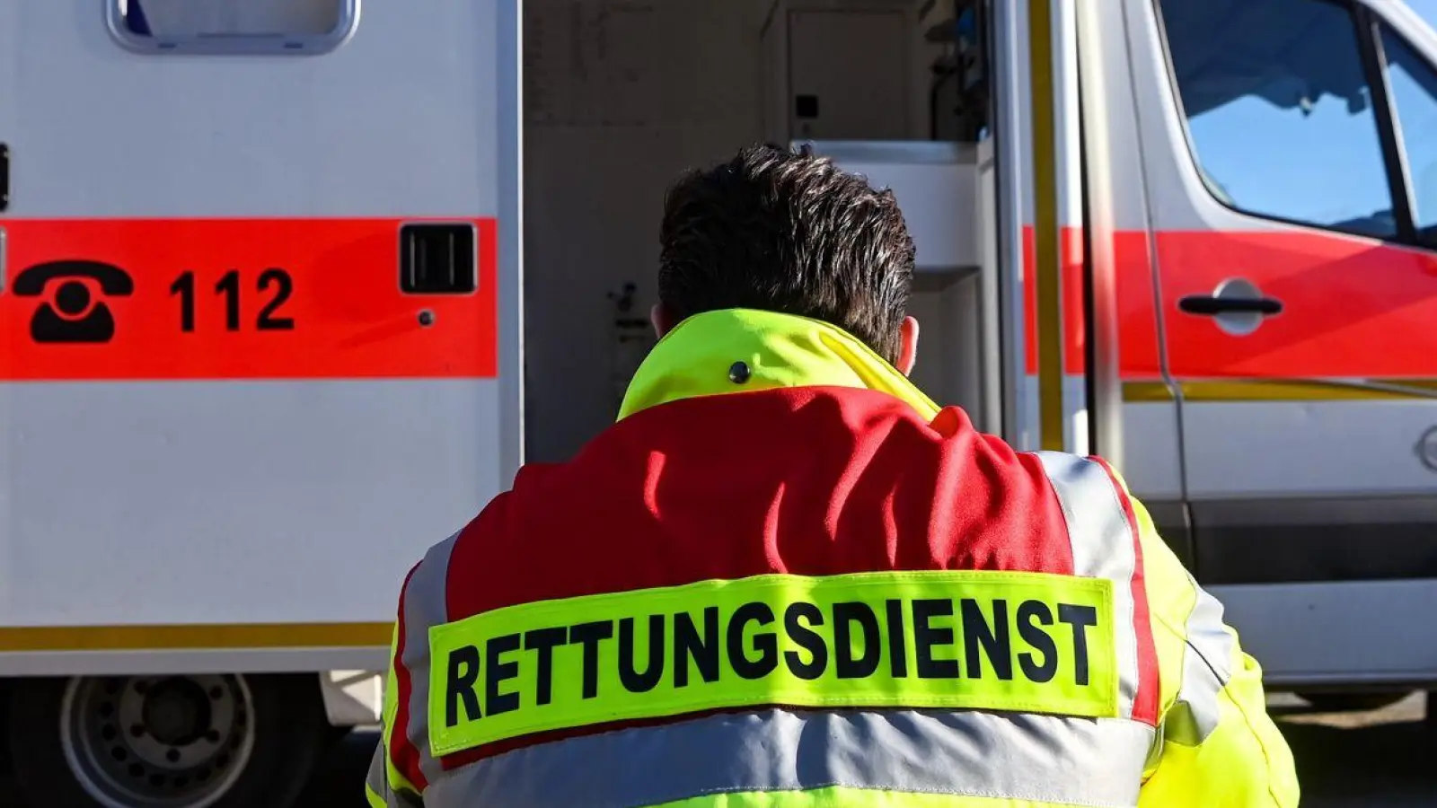 „Rettungsdienst“ steht auf der Jacke eines Mannes vor einem Rettungswagen der Feuerwehr. (Foto: Jens Kalaene/dpa/Symbolbild)