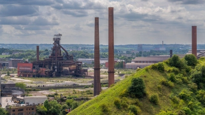 Industriegebiet von Charleroi: Blick über eine bewachsene Halde des Kohleabbaus am Wanderweg „Boucle Noire“, hinten Schornsteine und ein ehemaliger Hochofen eines Stahlwerks. (Foto: Oliver Gerhard/dpa-tmn)