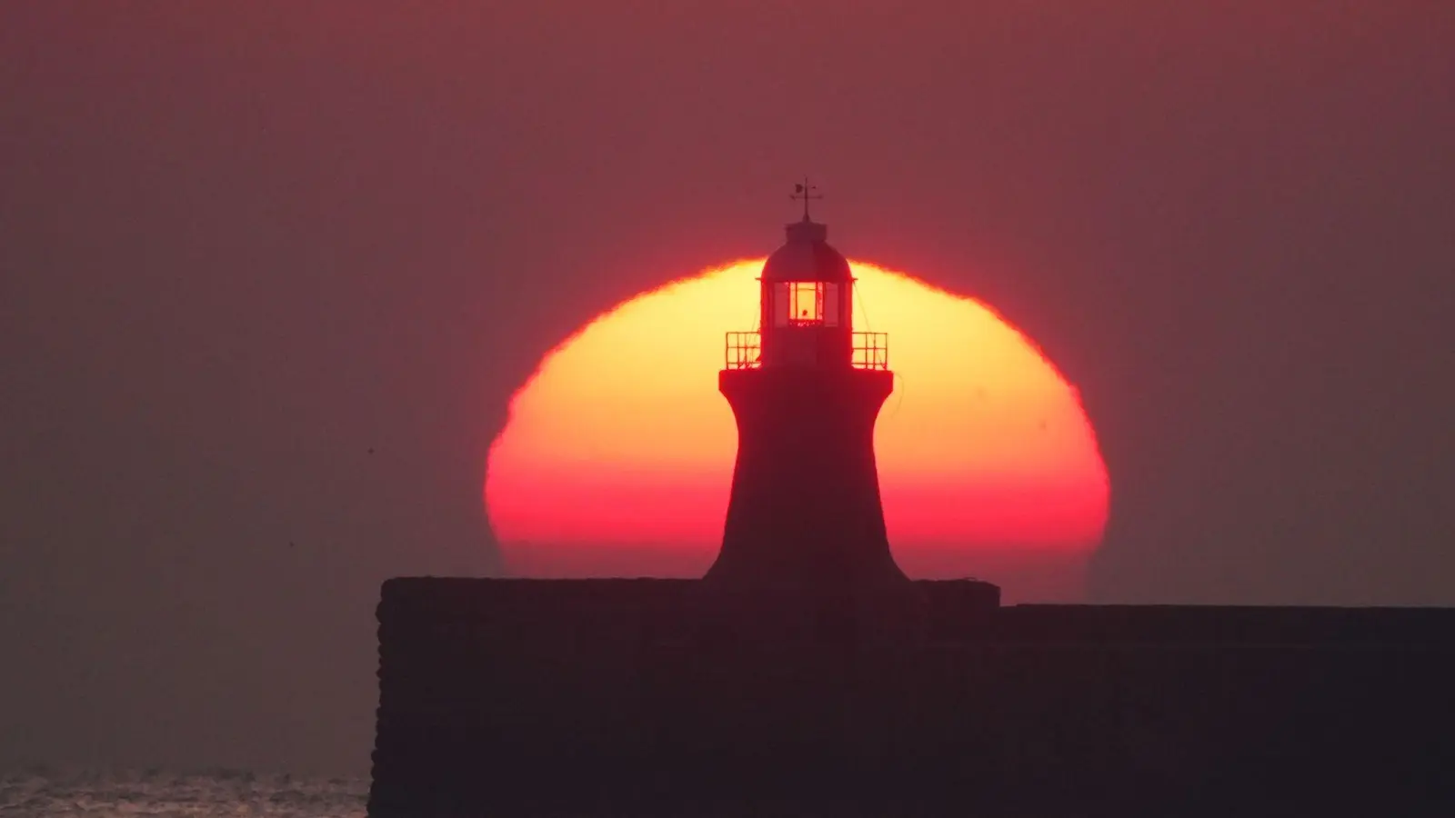 Die Sonne geht glutrot über dem Leuchtturm von South Shields an der Mündung des Flusses Tyne in Großbritannien auf. (Foto: Owen Humphreys/PA Wire/dpa)