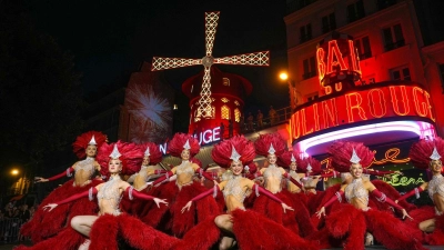 Moulin Rouge-Tänzerinnen und -Tänzer agieren vor den neuen Flügel der Windmühle des Moulin Rouge, die sich drehen, während das Kabarett in Paris seine Wiederinbetriebnahme feiert. Vierzehn Monate nach ihrem Sturz wurden die Flügel des Moulin Rouge wieder installiert und drehen sich nun wieder, womit eine mehr als 135 Jahre alte Tradition wiederbelebt wird. (Foto: Dimitar Dilkoff/AFP/dpa)