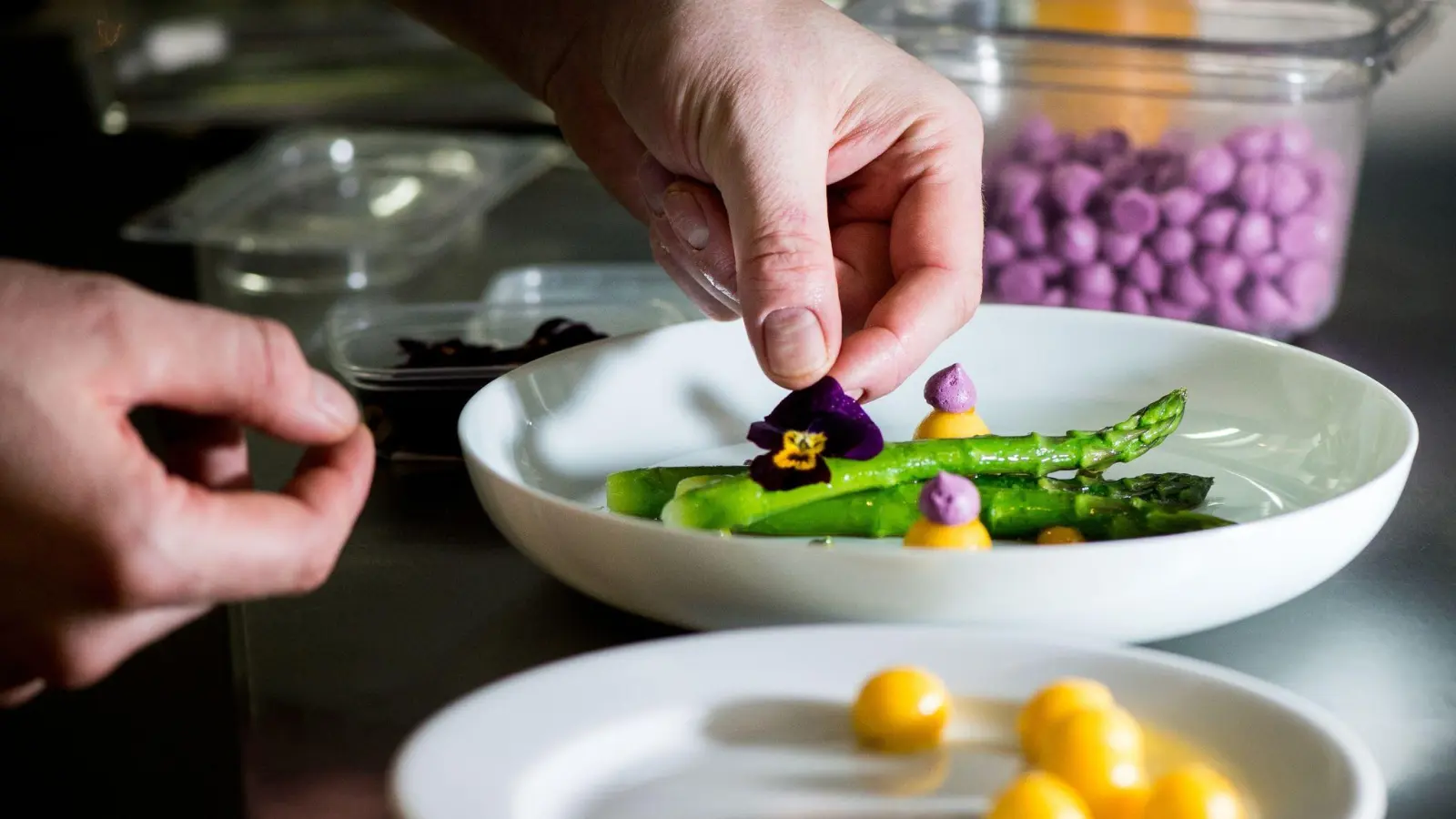 Lecker und schön anzusehen: Tim Raues Gericht mit grünem Spargel bekommt am Ende eine Veilchen-Dekoration. (Foto: Franziska Gabbert/dpa-tmn)