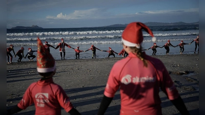 Mit Weihnachtsmannmützen verkleidete Menschen surfen während der „Papanoelada Surfera“ (Surfer-Nikolaus-Aktion) am Strand von Patos.  (Foto: Adrián Irago/EUROPA PRESS/dpa)