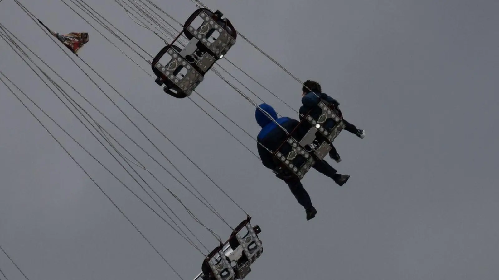 Besucher sitzen vor starkt bewölktem Himmel in einem Fahrgeschäft des Stuttgarter Frühlingsfestes. (Foto: Marijan Murat/dpa)