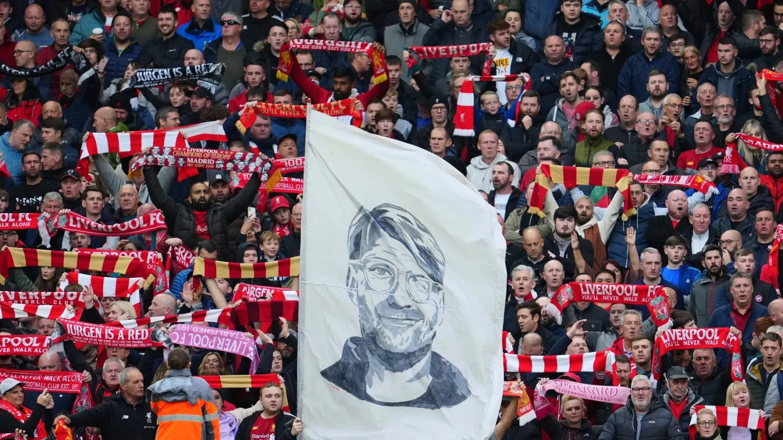 Liverpool-Fans präsentieren zur Unterstützung ihre Schals und halten ein Transparent mit einem Porträt von Trainer Jürgen Klopp. (Foto: Jon Super/AP/dpa)