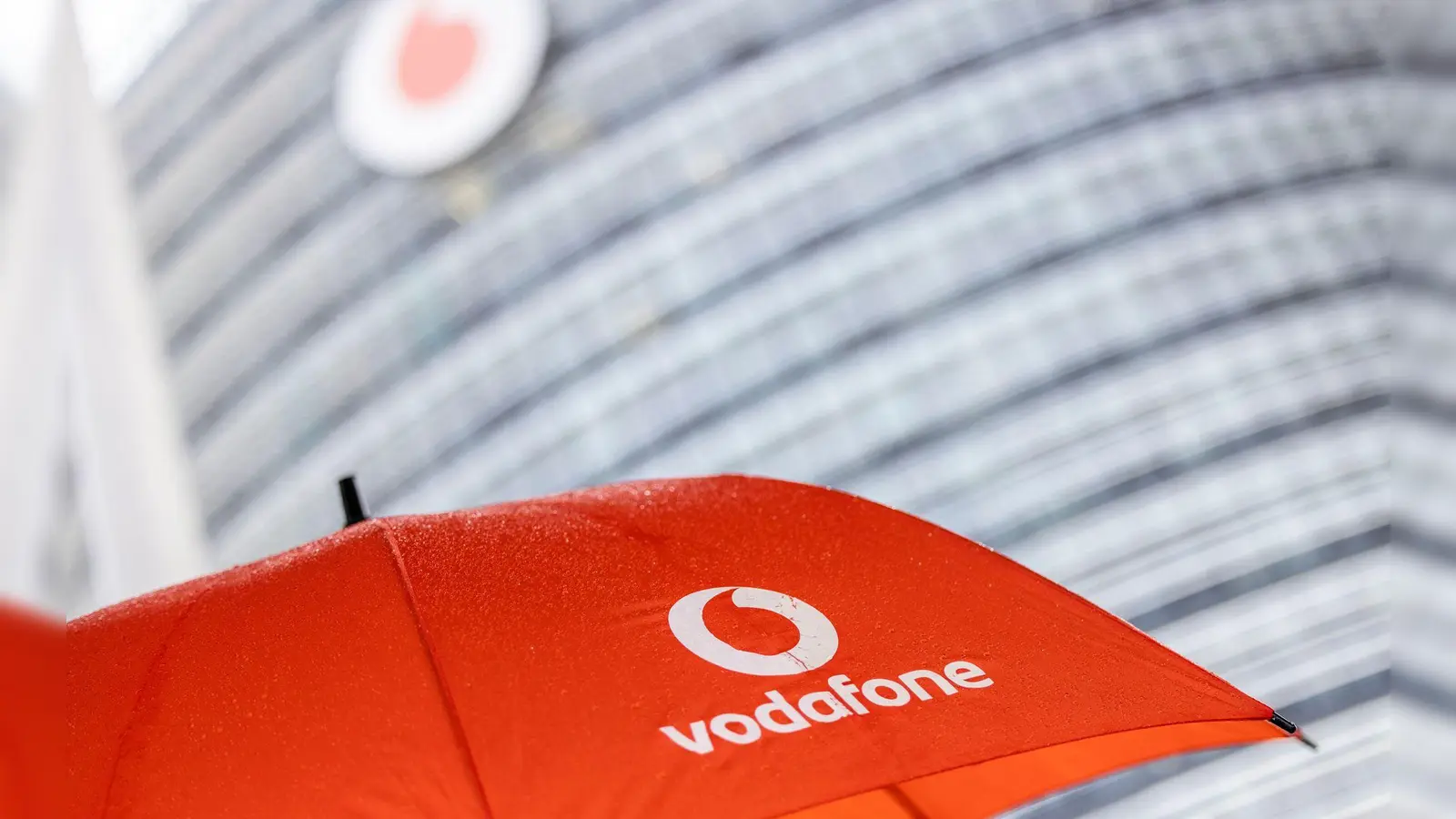 Ein Passant geht mit einem aufgespanntem Regenschirm mit dem Logo von Vodafone an der Zentrale der Deutschlandtochter des britischen Vodafone-Konzerns vorbei. (Foto: Thomas Banneyer/dpa)