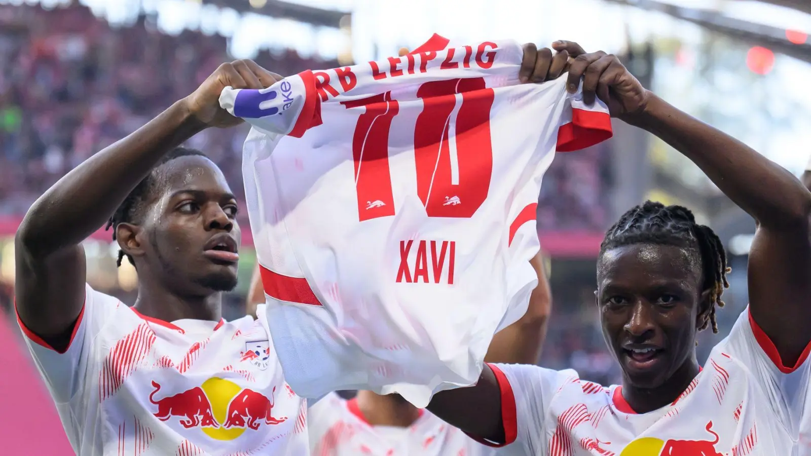 Leipzigs Castello Lukeba (l) und Amadou Haidara halten nach dem 2:1 ein Trikot des verletzten Xavi Simons nach oben. (Foto: Hendrik Schmidt/dpa)