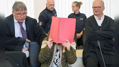 Die Angeklagte sitzt mit Aktendeckel vor dem Gesicht zwischen ihren Verteidigern Andreas Ohm (l-r) und Thomas Löcker.  (Foto: Bernd Wüstneck/dpa)
