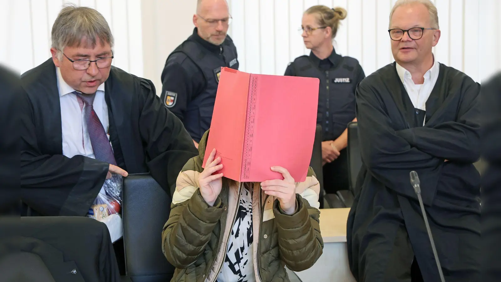 Die Angeklagte sitzt mit Aktendeckel vor dem Gesicht zwischen ihren Verteidigern Andreas Ohm (l-r) und Thomas Löcker.  (Foto: Bernd Wüstneck/dpa)